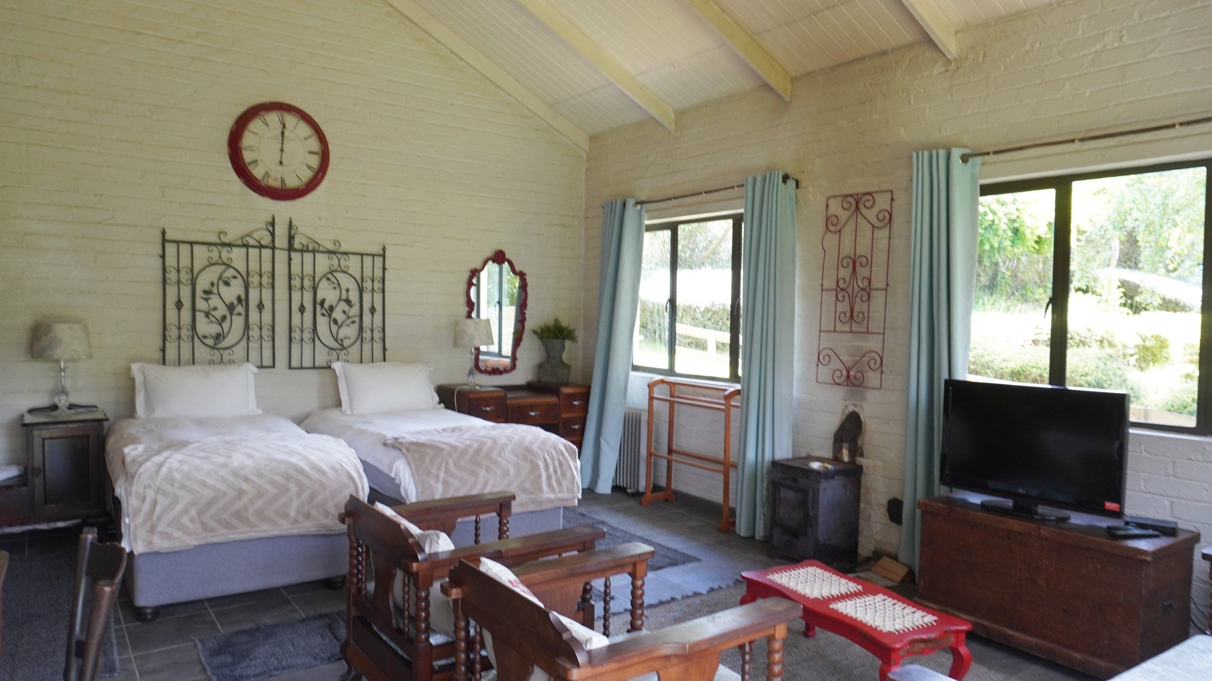 Inside The Bird House: two single beds under a vaulted ceiling, with a wood-burning stove and windows onto the garden