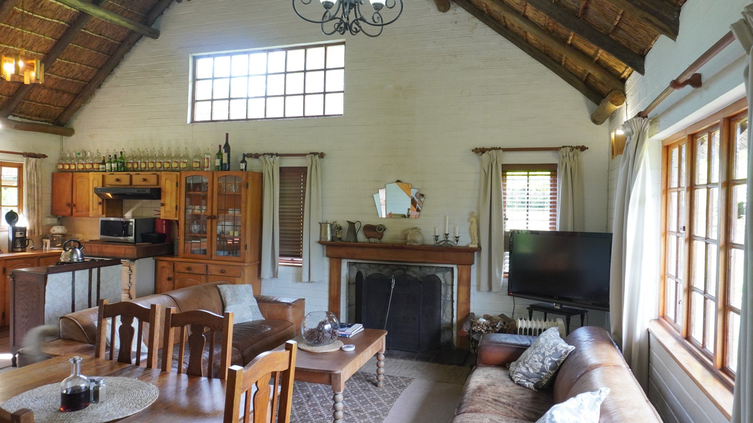 De-vine View's open-plan living room under the thatch: the pine kitchen and dresser, dining table, fireplace, leather sofas and a high window